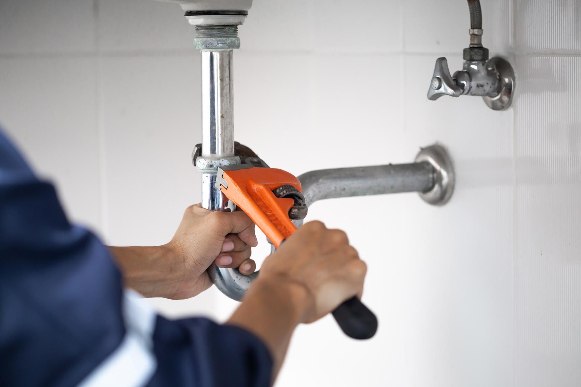 Hands of plumbing repair contractors using a wrench under a sink.