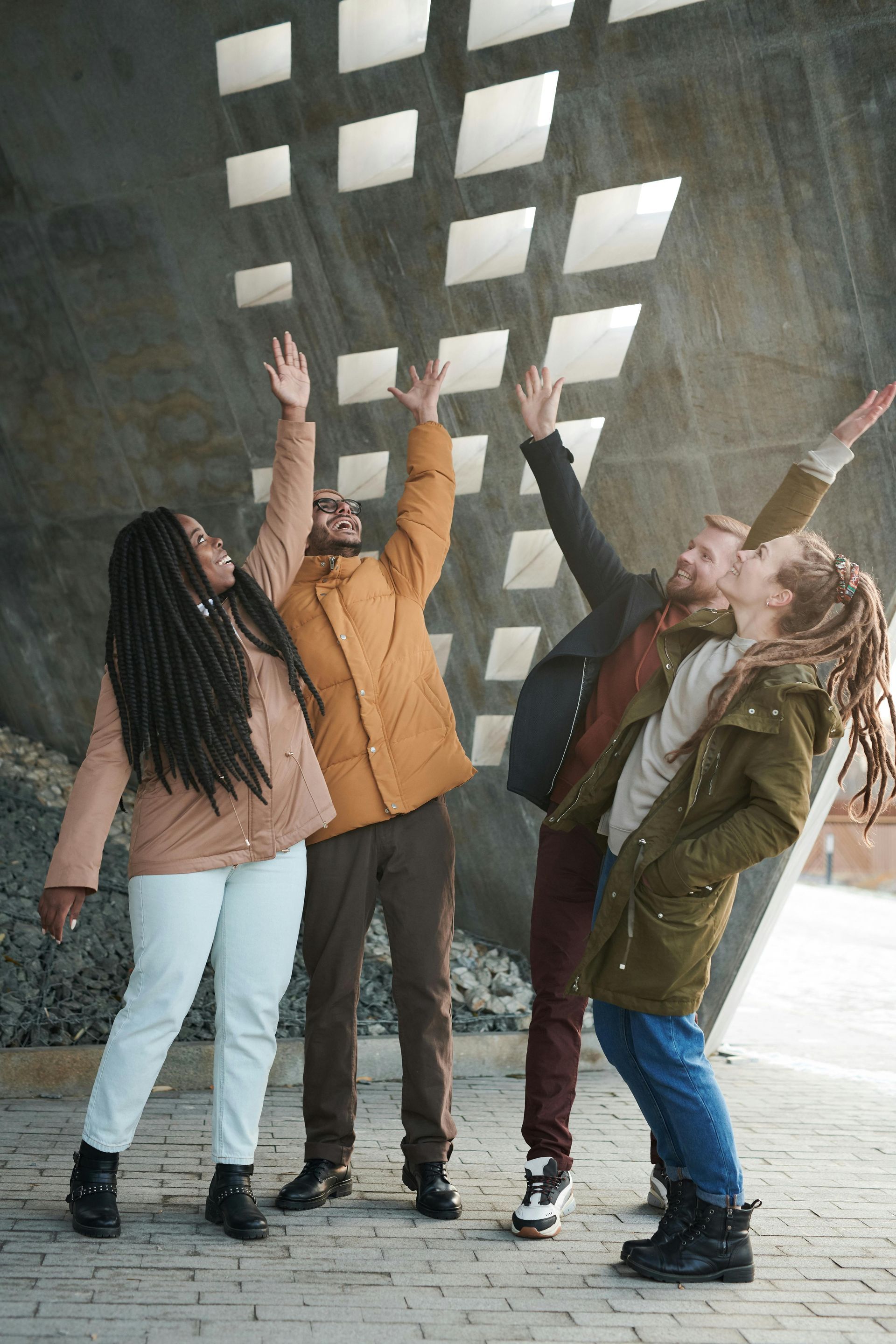 Four people raise arms to sunlight streaming through a geometric wall. Teamwork, community, healing, transformation, health care providers, health care professionals