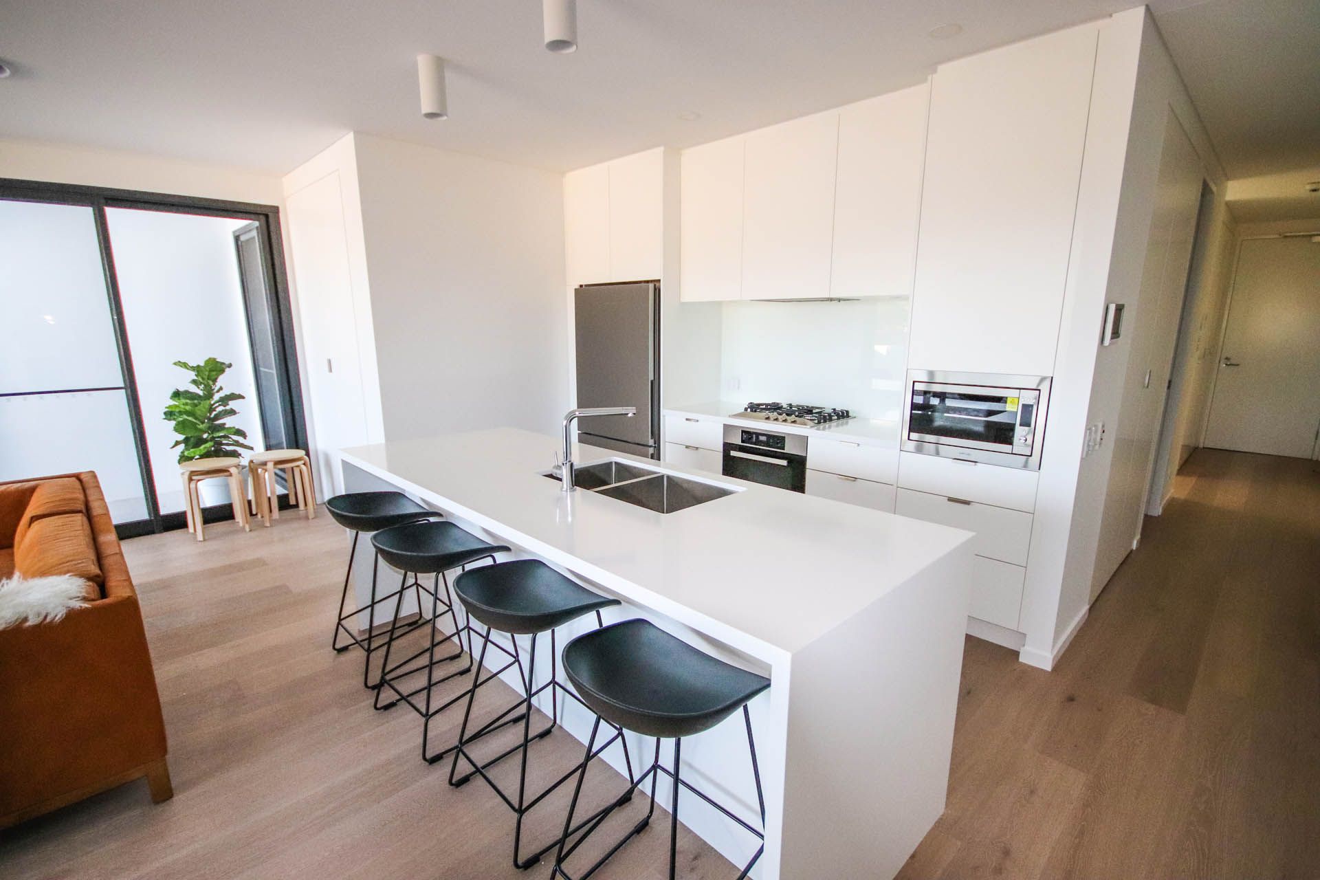 Modern kitchen with white cabinets, island with stools, and appliances. Wooden floor and balcony— Ray Smith Electrical in Korora, NSW