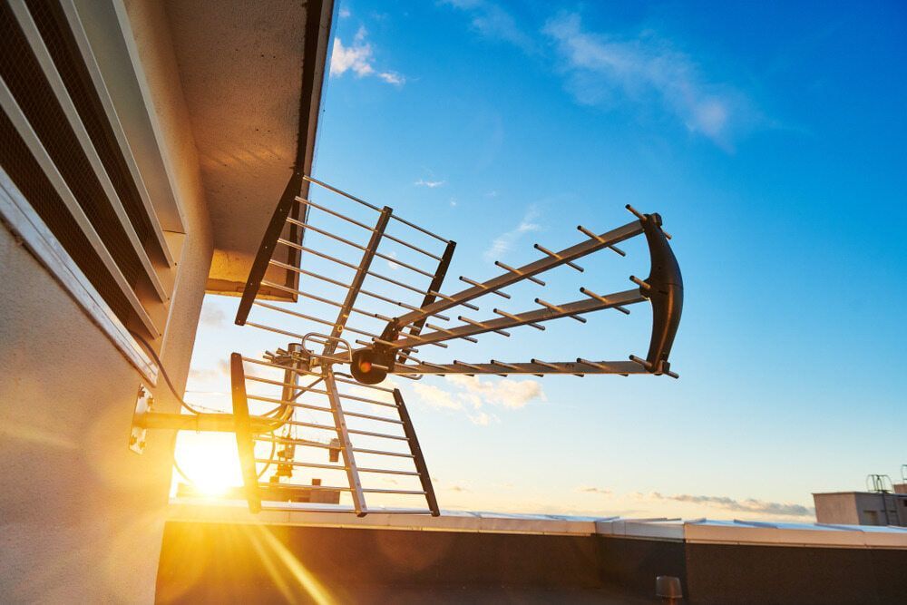 A Large Antenna is Hanging From the Side of a Building at Sunset — Ray Smith Electrical in Korora, NSW