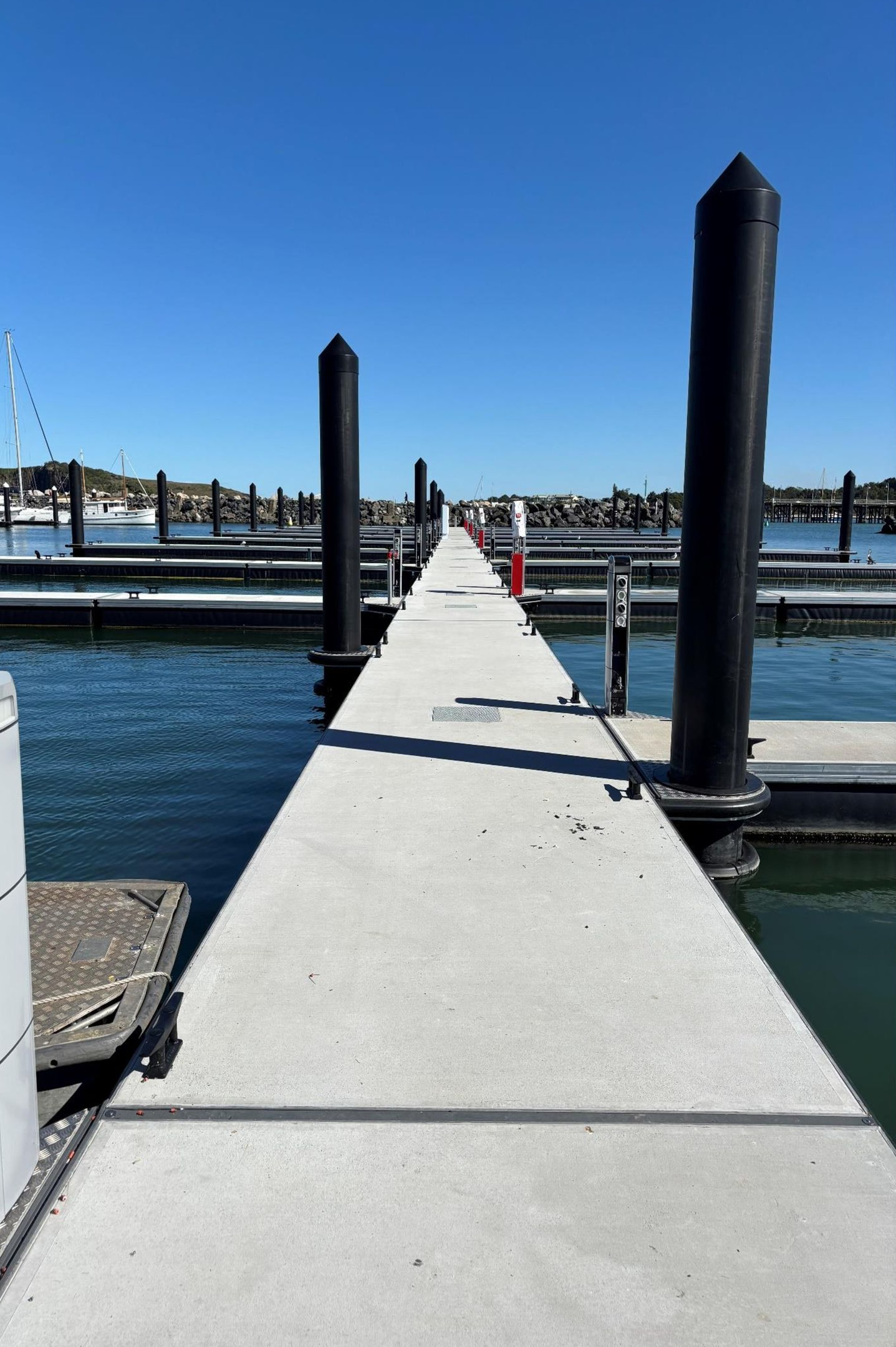 Concrete dock stretching into distance, black pilings, water on sides, blue sky— Ray Smith Electrical in Korora, NSW