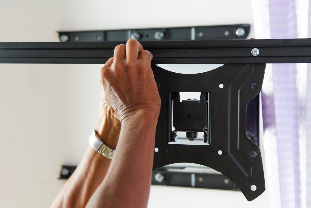 A Person is Installing a Flat Screen Tv Mount on a Wall — Ray Smith Electrical in Korora, NSW
