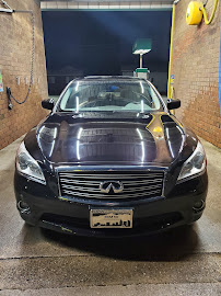 Black Infiniti sedan at a car wash, night. Wet pavement, dark background.