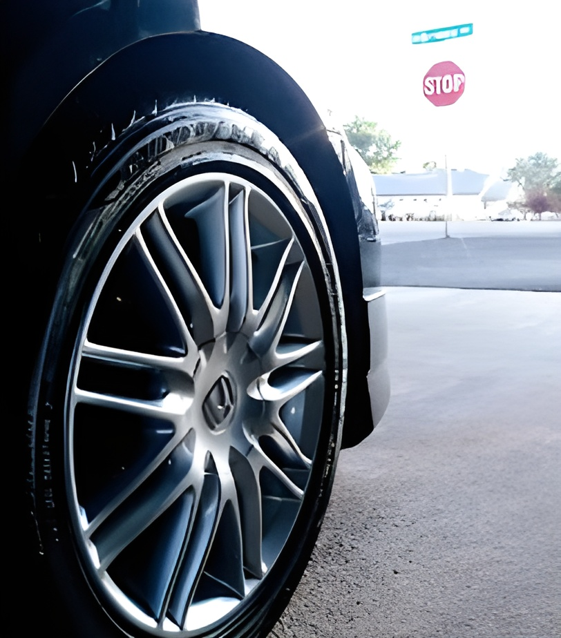 Shiny black car wheel with silver spokes, by a stop sign.