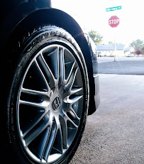Close-up of a shiny black car tire with a silver rim; a stop sign is in the background.