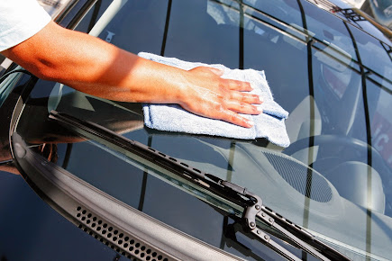 Person cleaning a car windshield with a blue cloth.