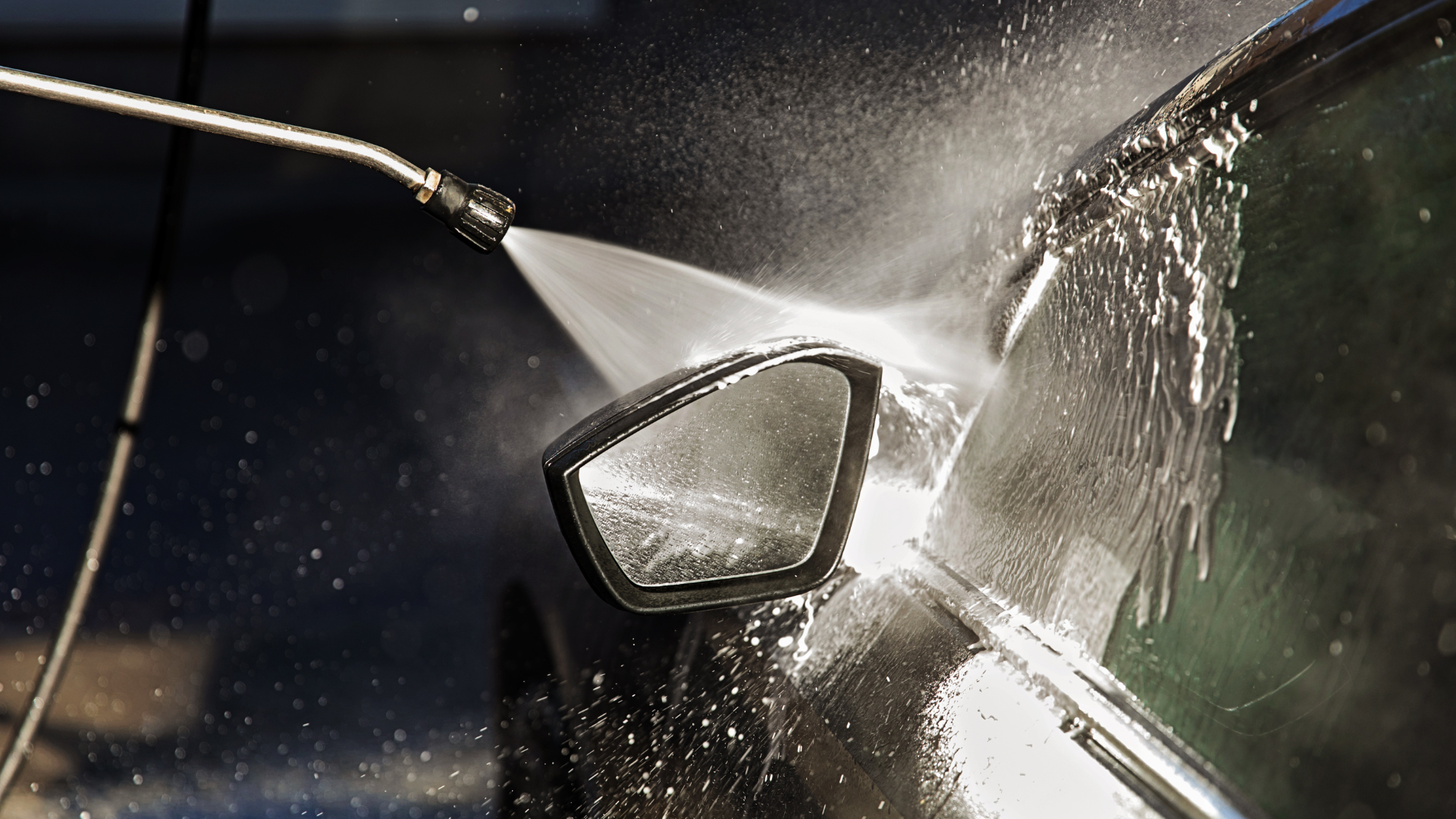 A car side mirror being sprayed with water from a pressure washer.