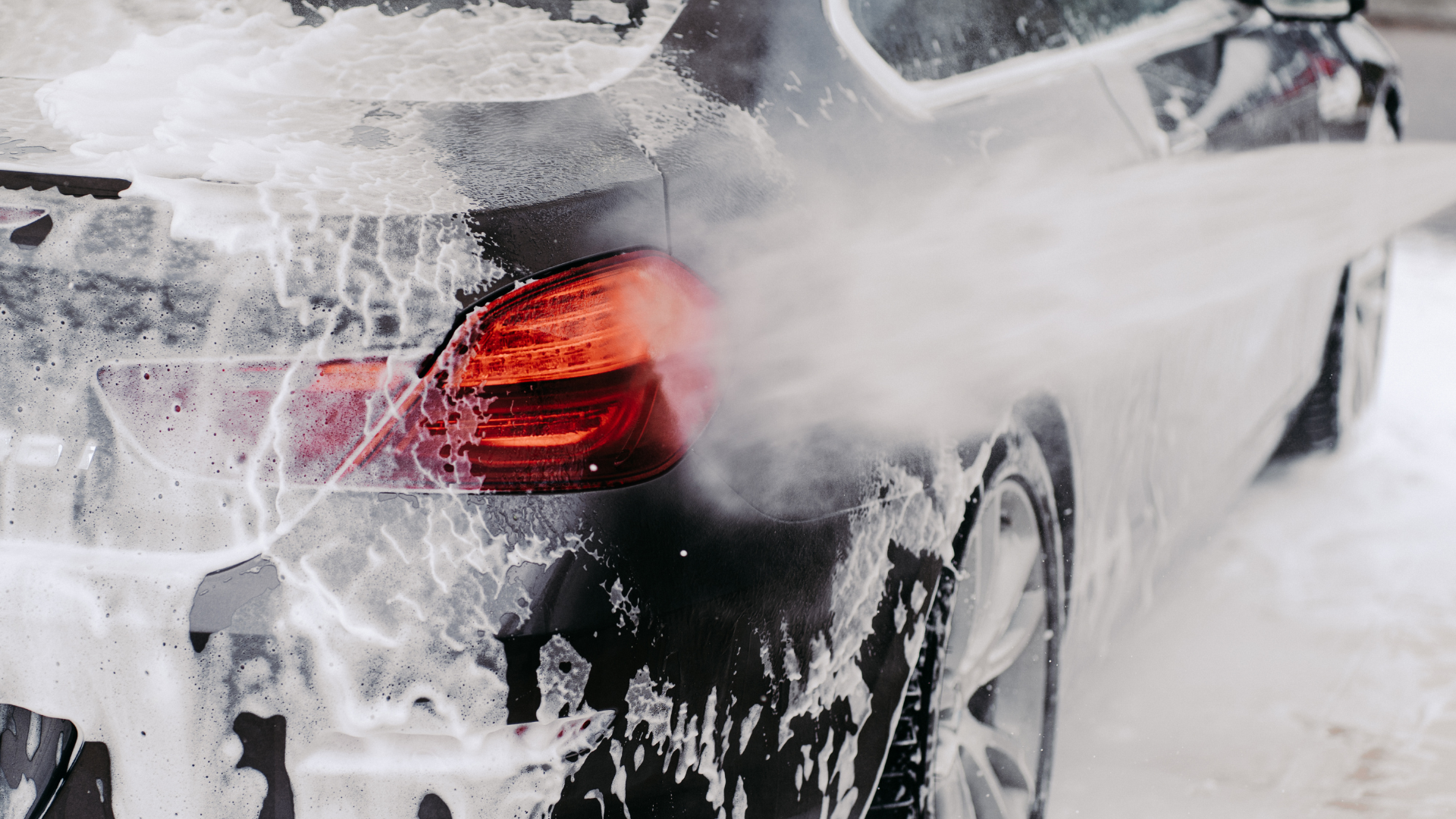 Car being washed with foamy soap spray.