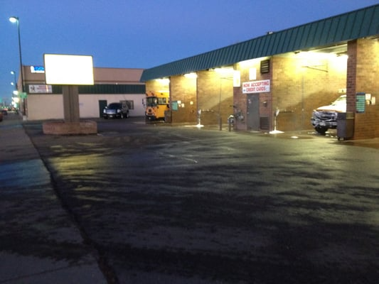 A car wash at dusk; the building is brick with green trim, and there are two vehicles being cleaned.