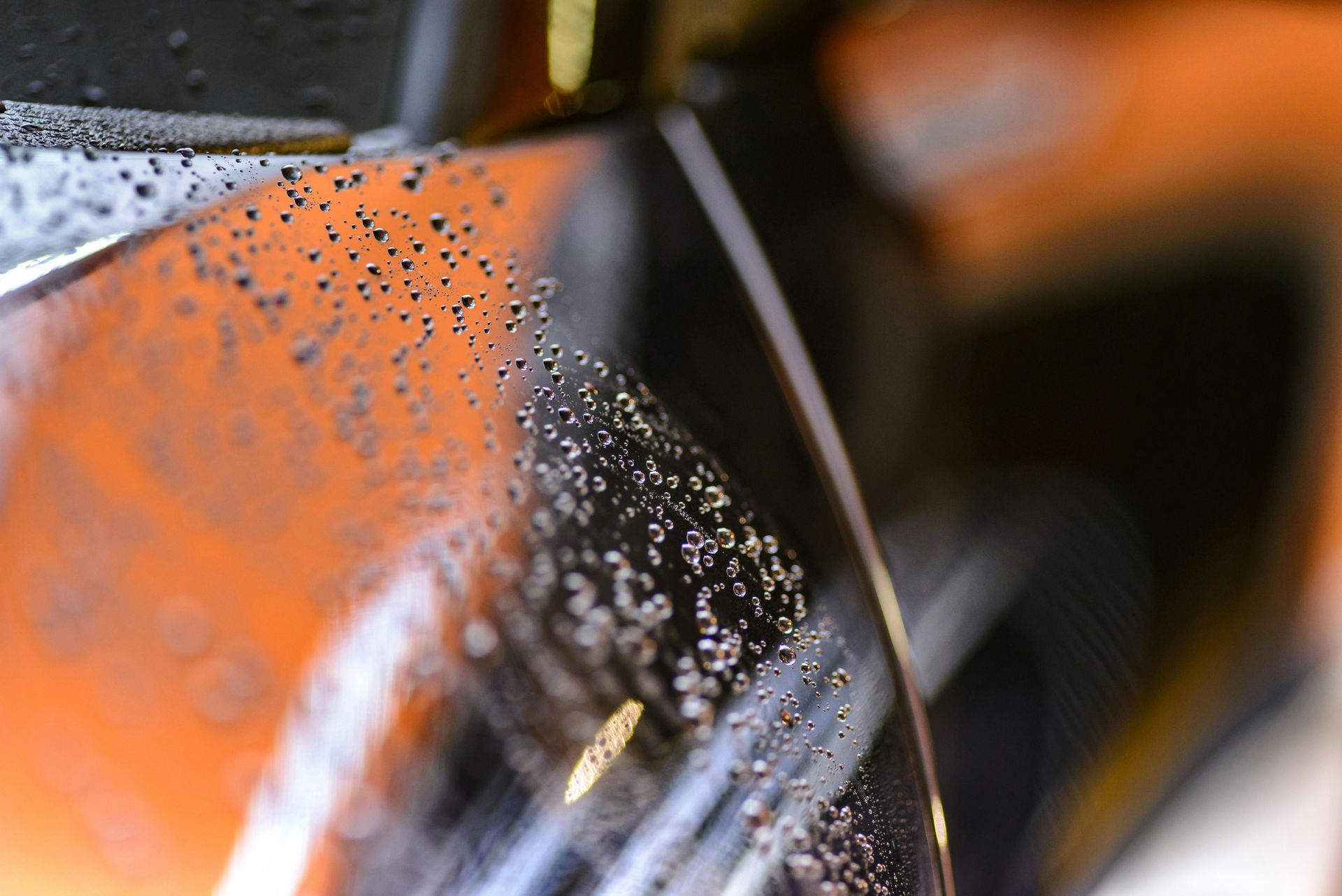 Close-up of a glossy, dark surface with water droplets, reflecting an orange object.