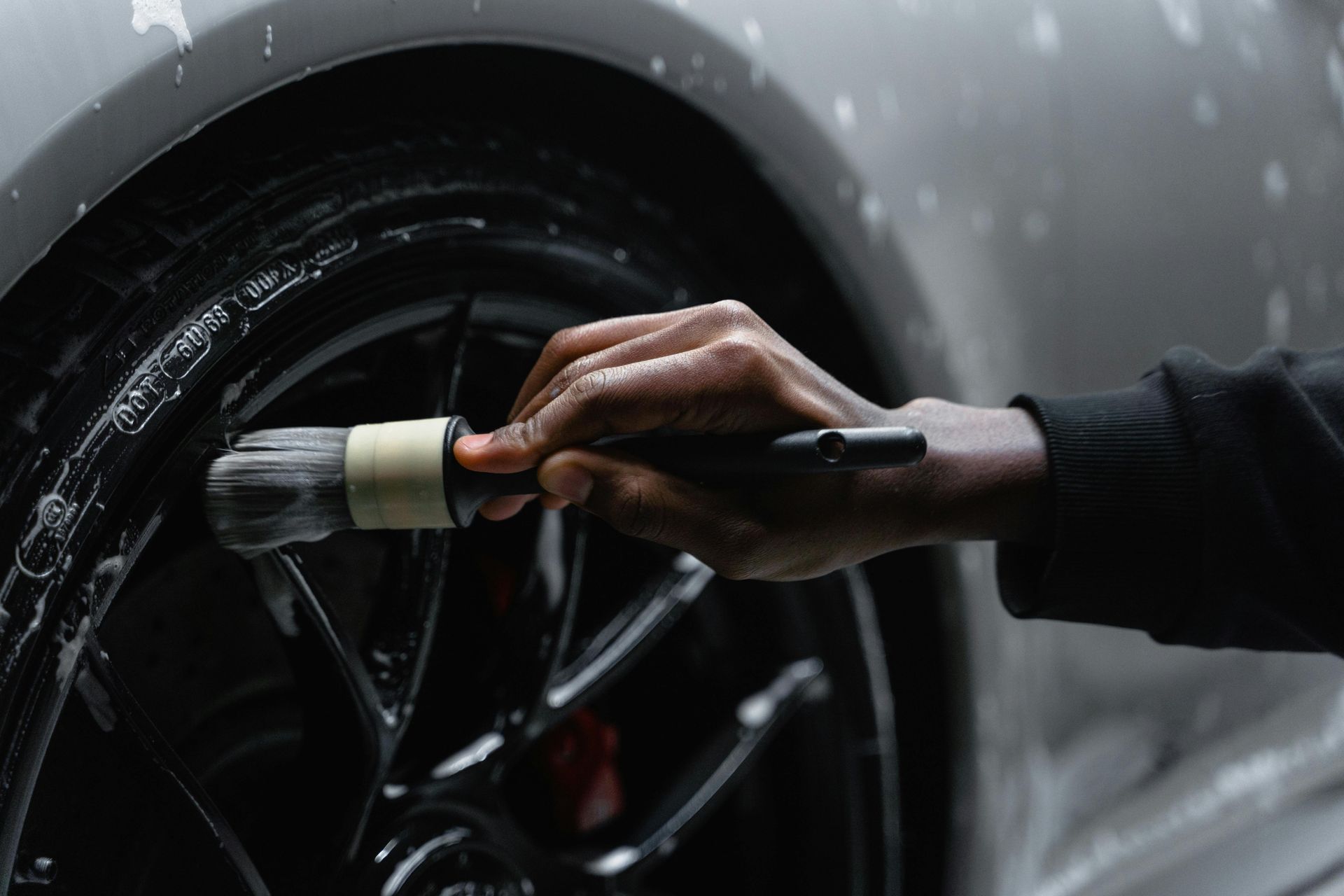 Person cleaning a black car wheel with a brush and soap.