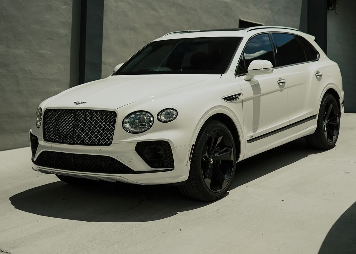 A white Bentley Bentayga is parked in front of a building.