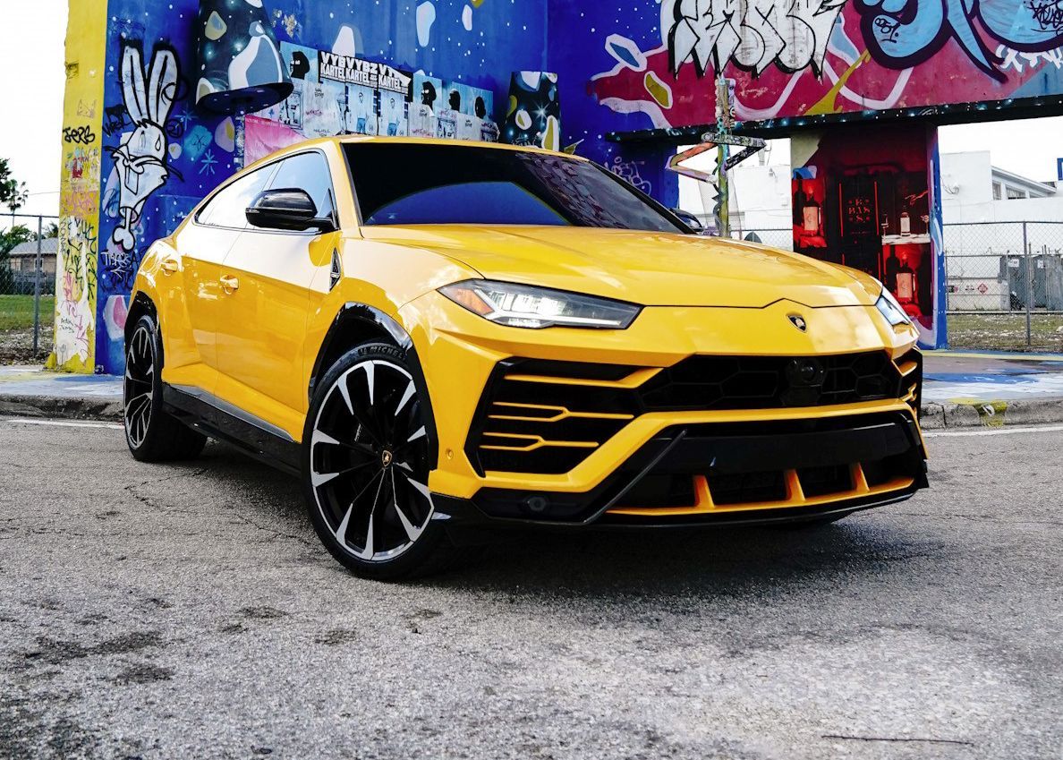 A yellow Lamborghini Urus is parked in front of a graffiti covered building.