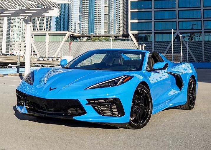 A blue sports car is parked in a parking lot in front of a building.