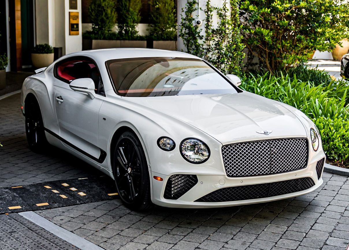 A white Bentley Continental GT is parked in a parking lot.