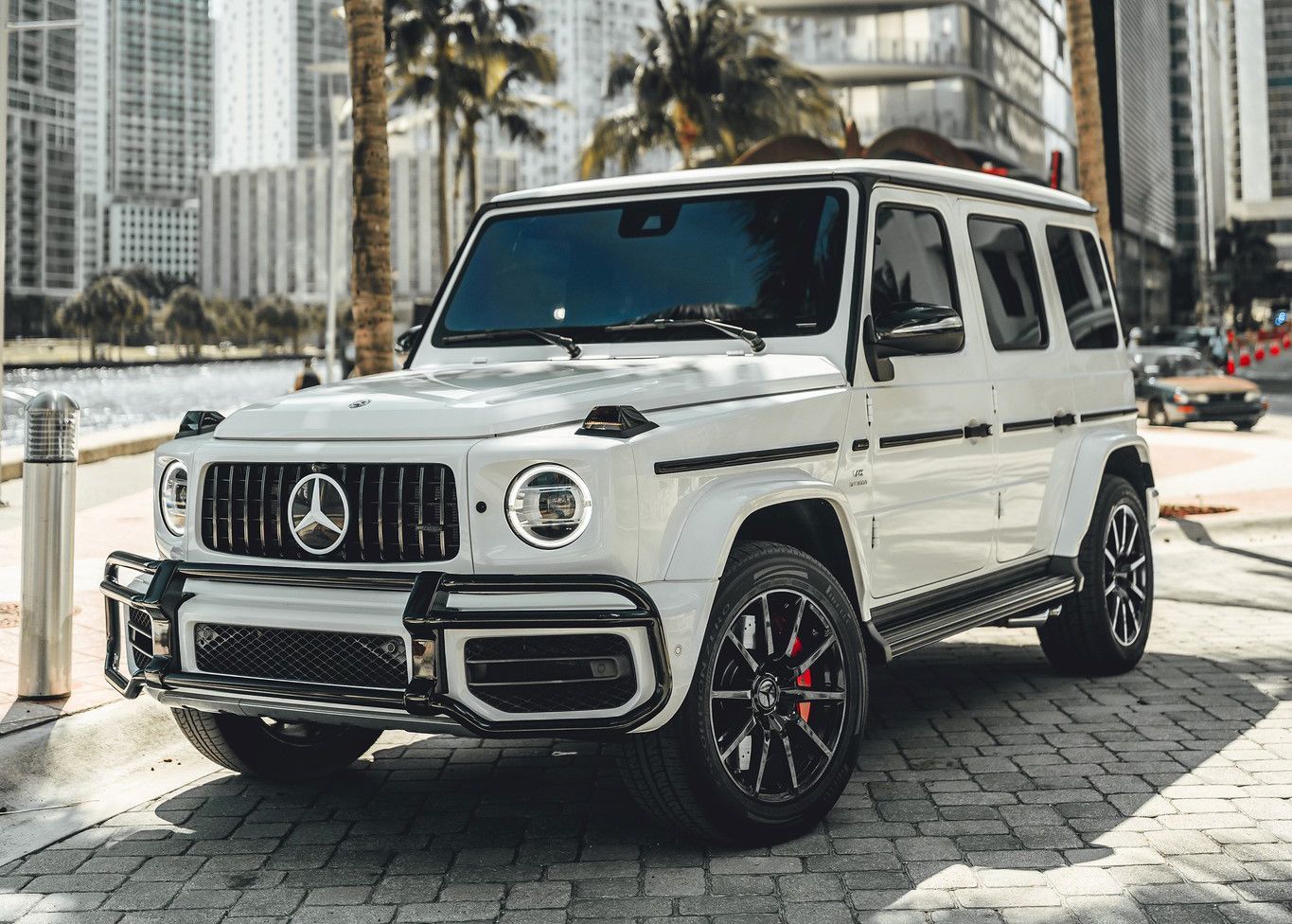 A white Mercedes Benz is parked on a brick sidewalk in front of a city.