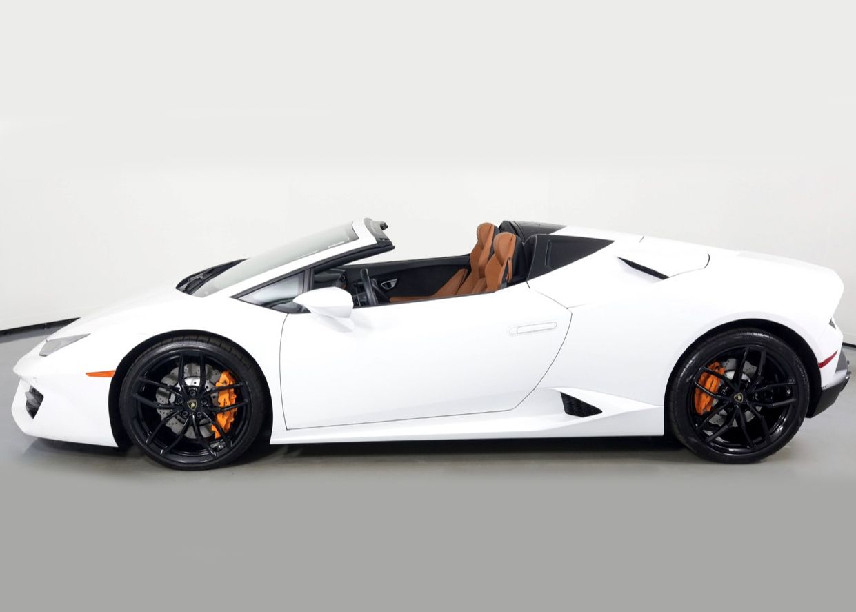 A white Lamborghini Huracan Roadster is parked on a gray surface.
