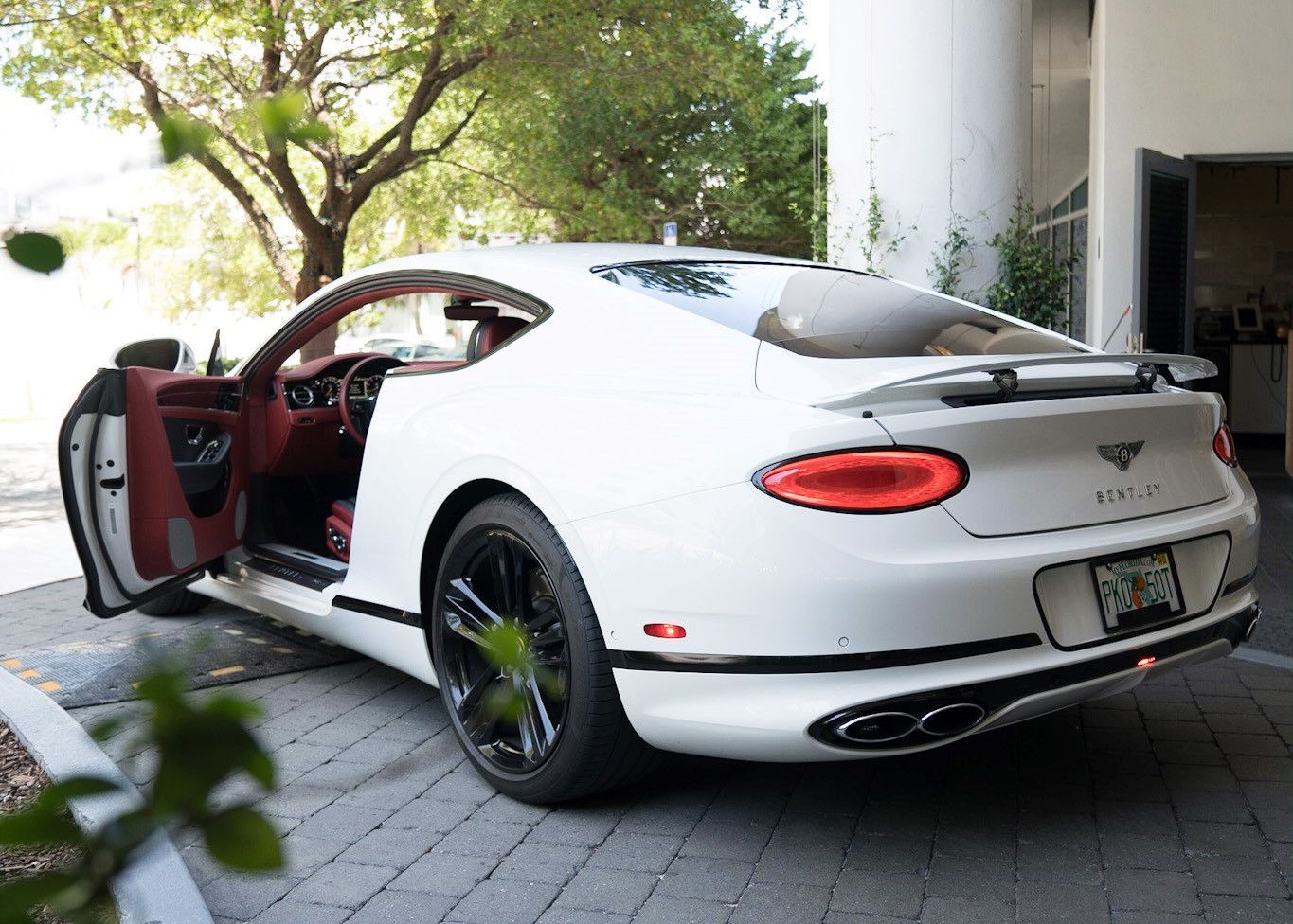 A white Bentley Continental GT is parked in a driveway with its door open.