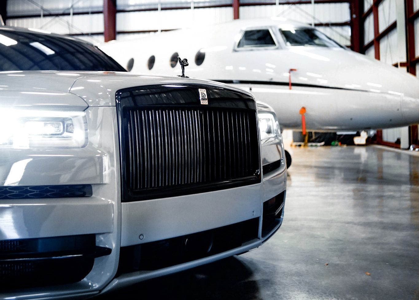 A white car is parked next to a private jet in a hangar.