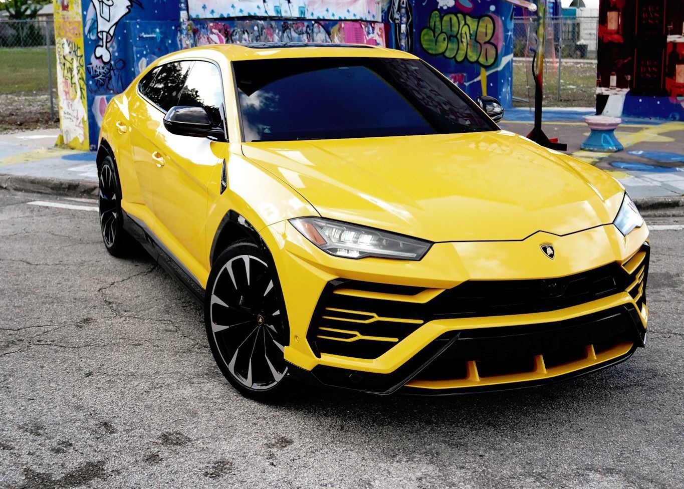 A yellow Lamborghini Urus is parked in front of a graffiti covered wall.