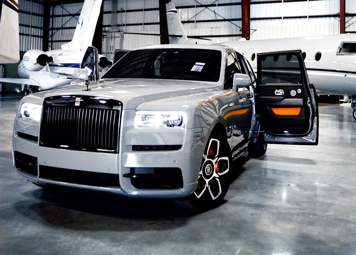 A silver Rolls Royce is parked in a hangar next to a private jet.