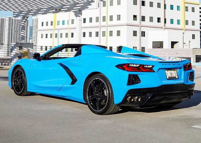 A blue sports car is parked in a parking lot in front of a building.