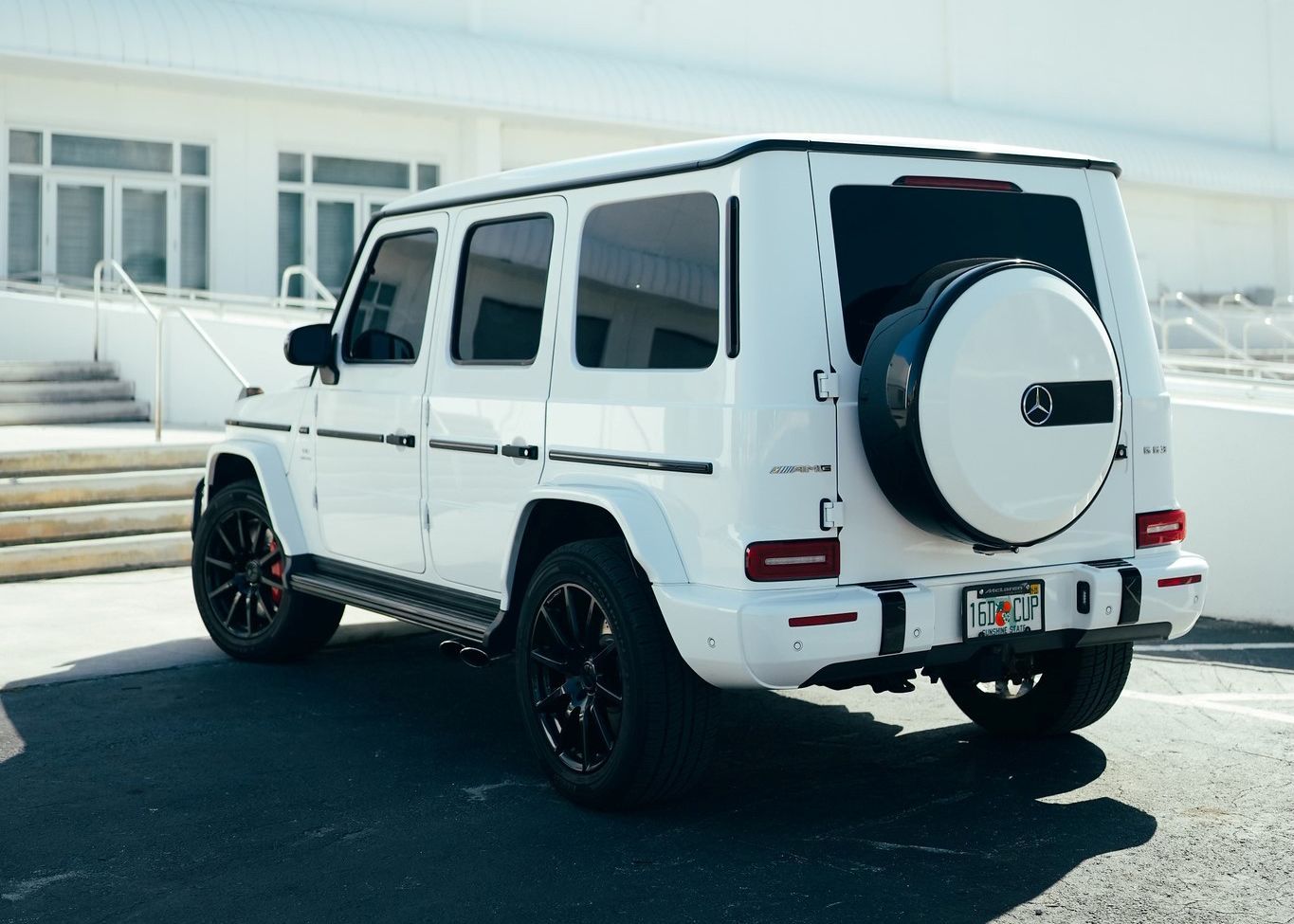 A white Mercedes Benz G550 is parked in a parking lot in front of a building.