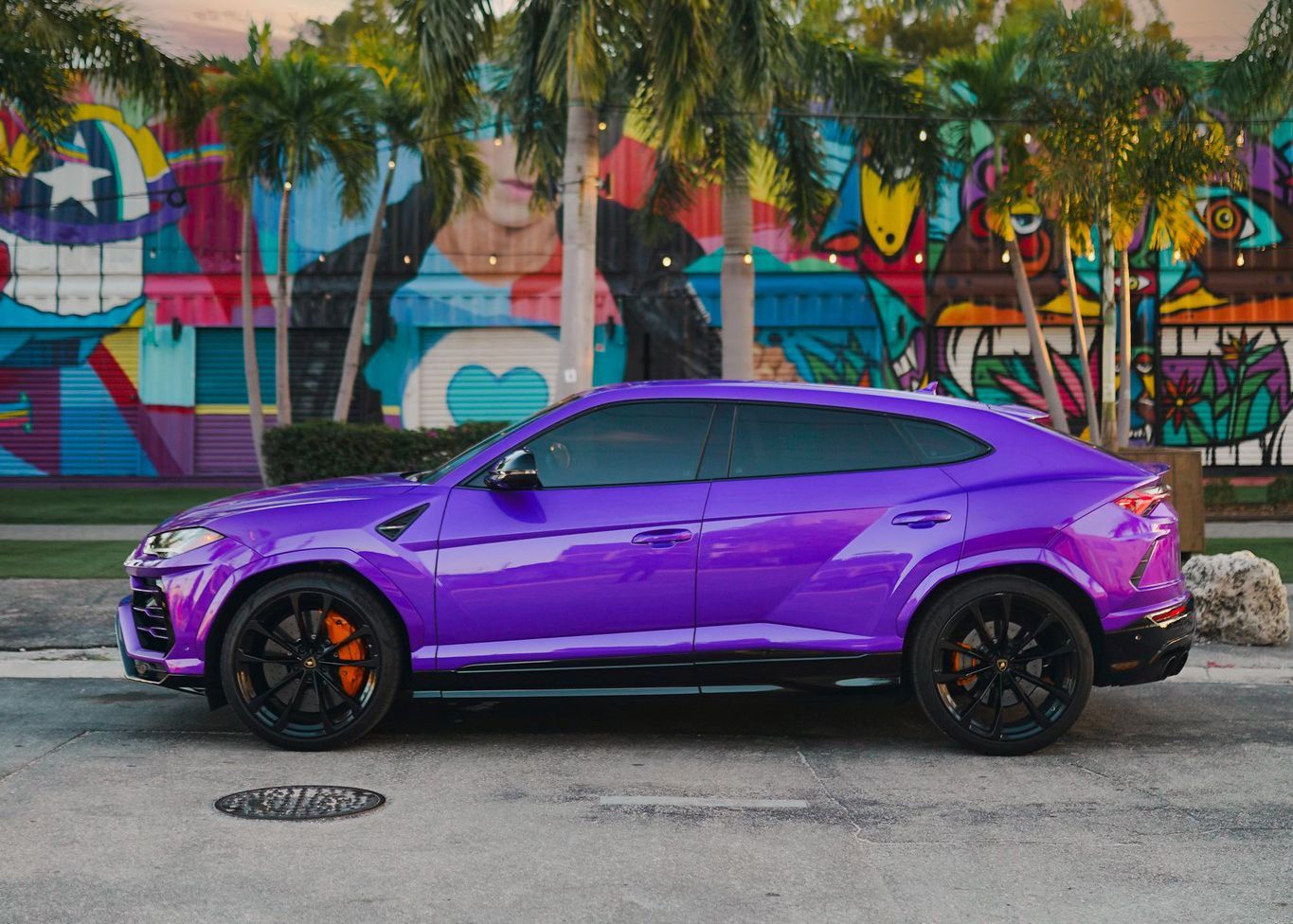 A purple Lamborghini Urus is parked in front of a graffiti covered wall.