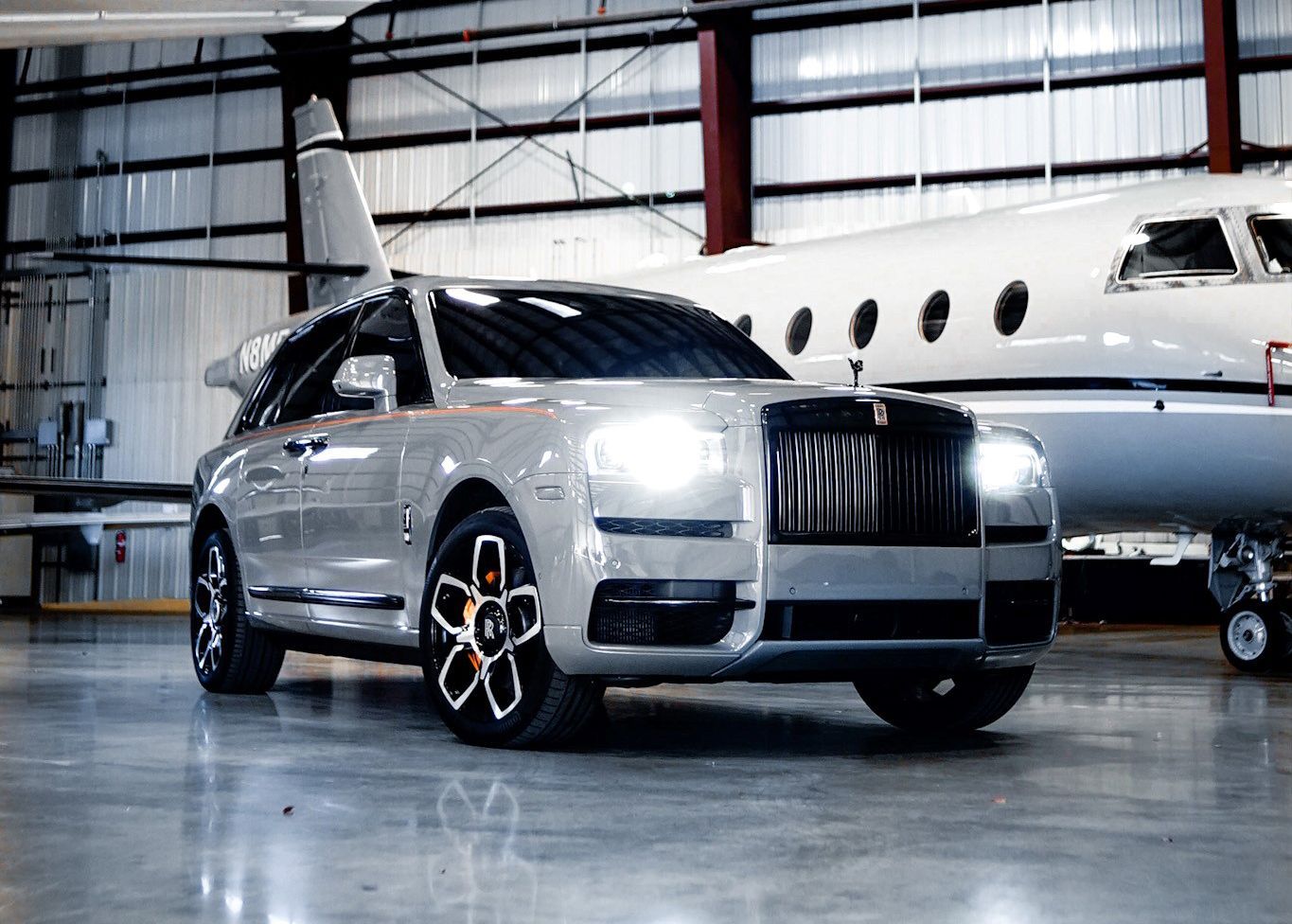 A silver car is parked next to a private jet in a hangar.