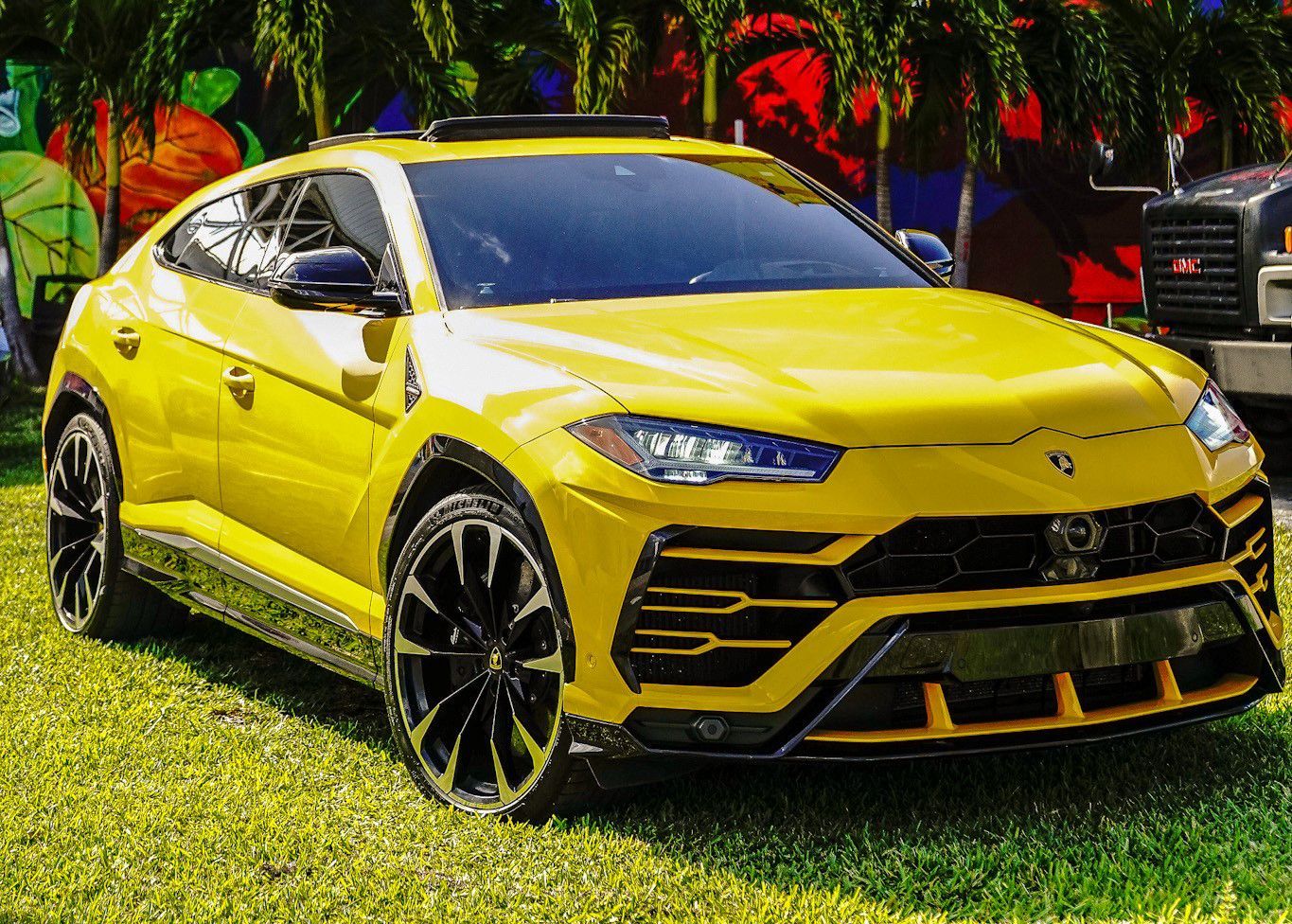 A yellow Lamborghini Urus is parked in the grass.