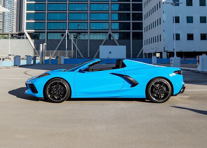 A blue sports car is parked in a parking lot in front of a building.