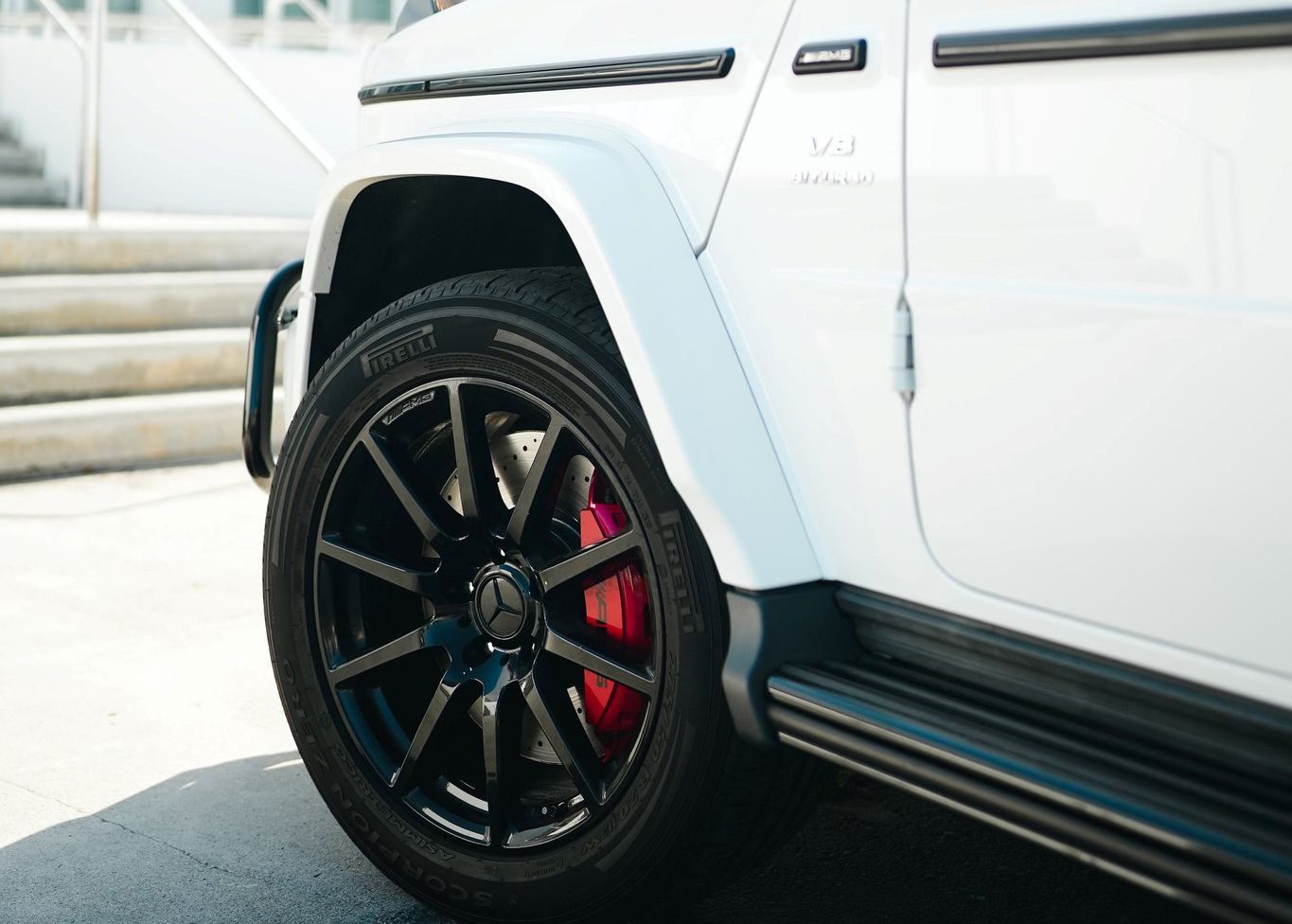 A white Mercedes Benz G550 with black wheels and red brake calipers is parked on the side of the road.