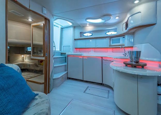 A kitchen on a boat with a blue pillow on the couch.