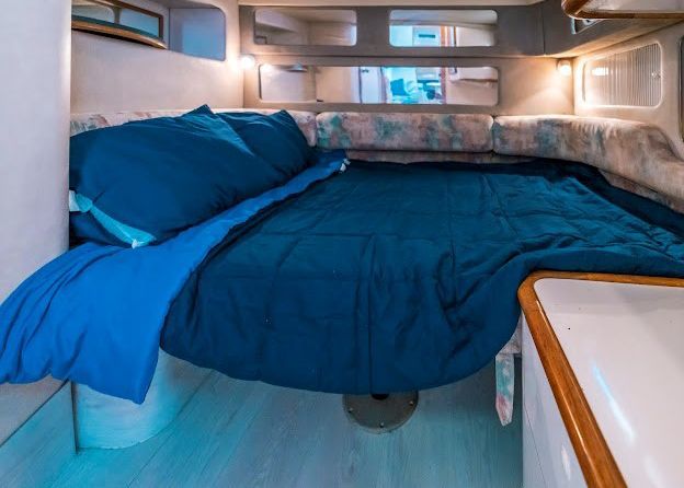 A bed in a boat with a blue comforter and pillows.