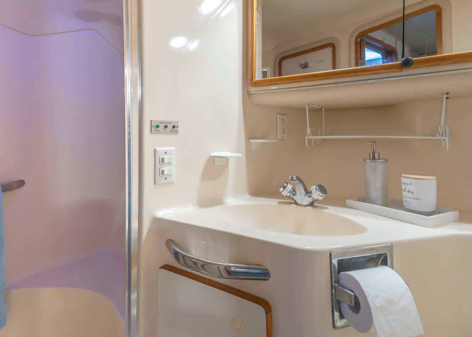 A bathroom with a sink , toilet paper, mirror and shower.