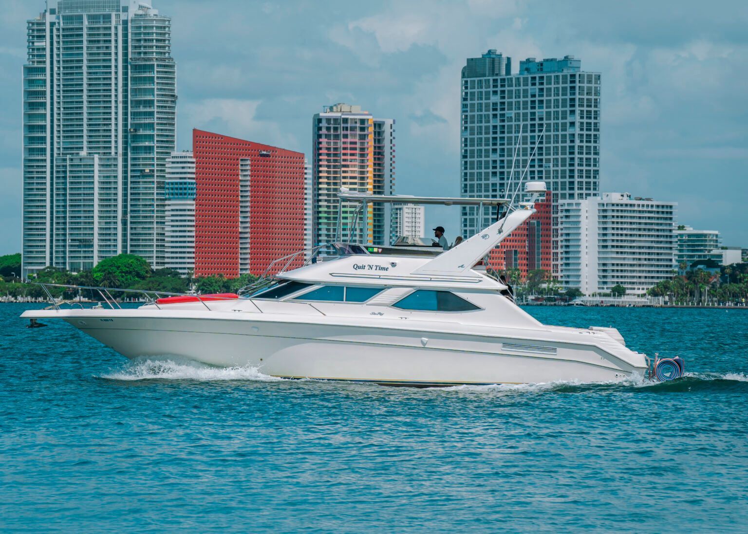 A white yacht is floating on top of a body of water in front of a city skyline.