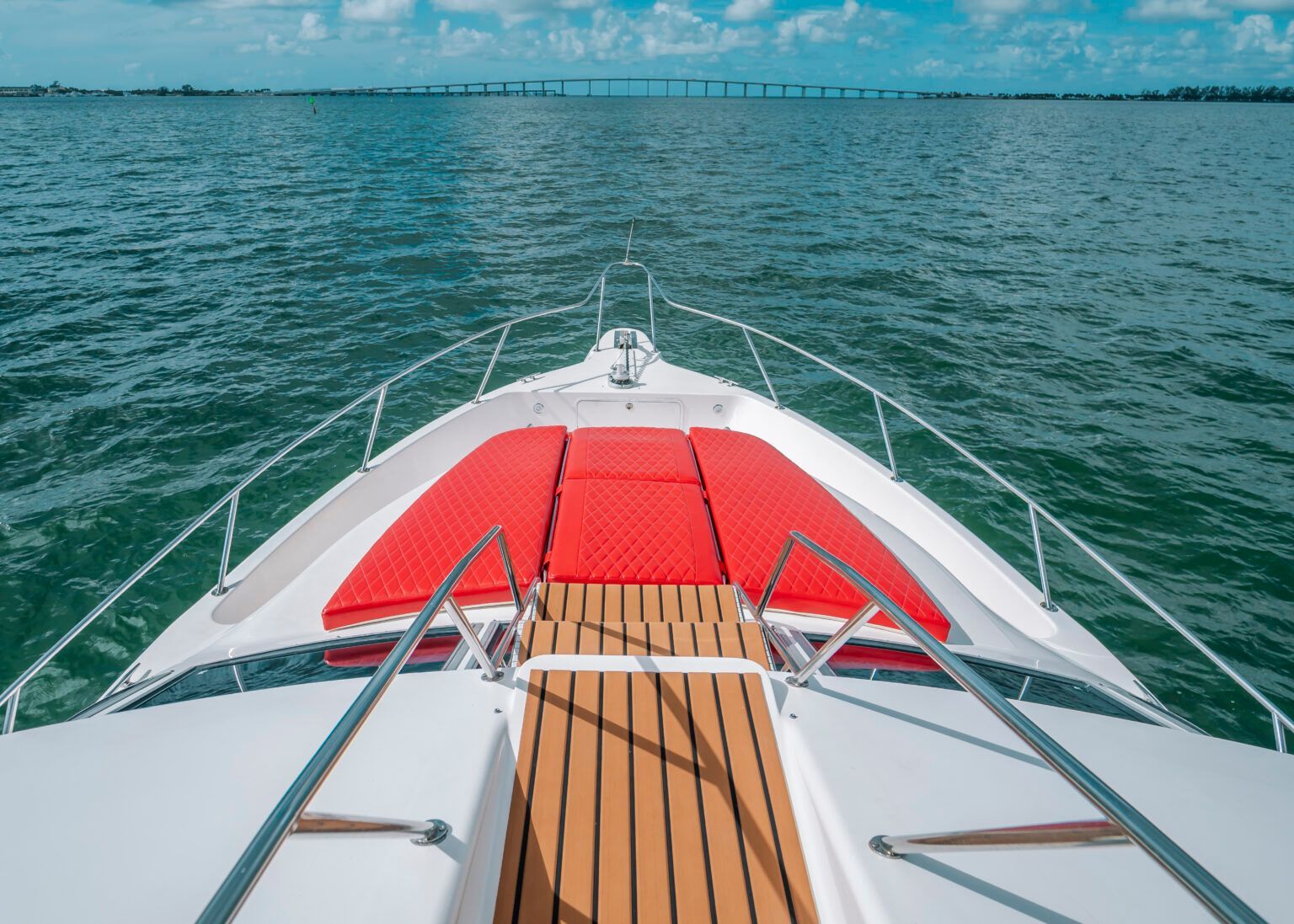 The front of a white boat with a red cushion on the bow is floating on top of a body of water.