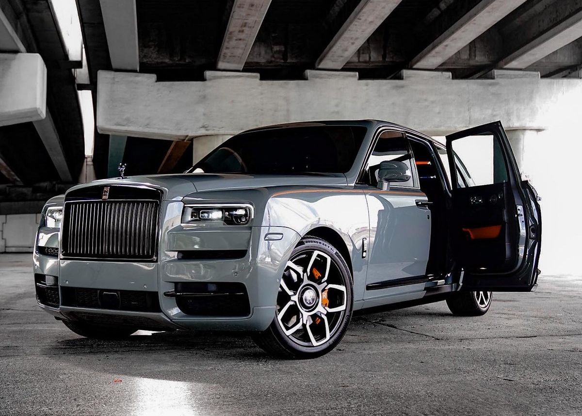 A gray Rolls Royce Cullinan is parked under a bridge with its doors open.