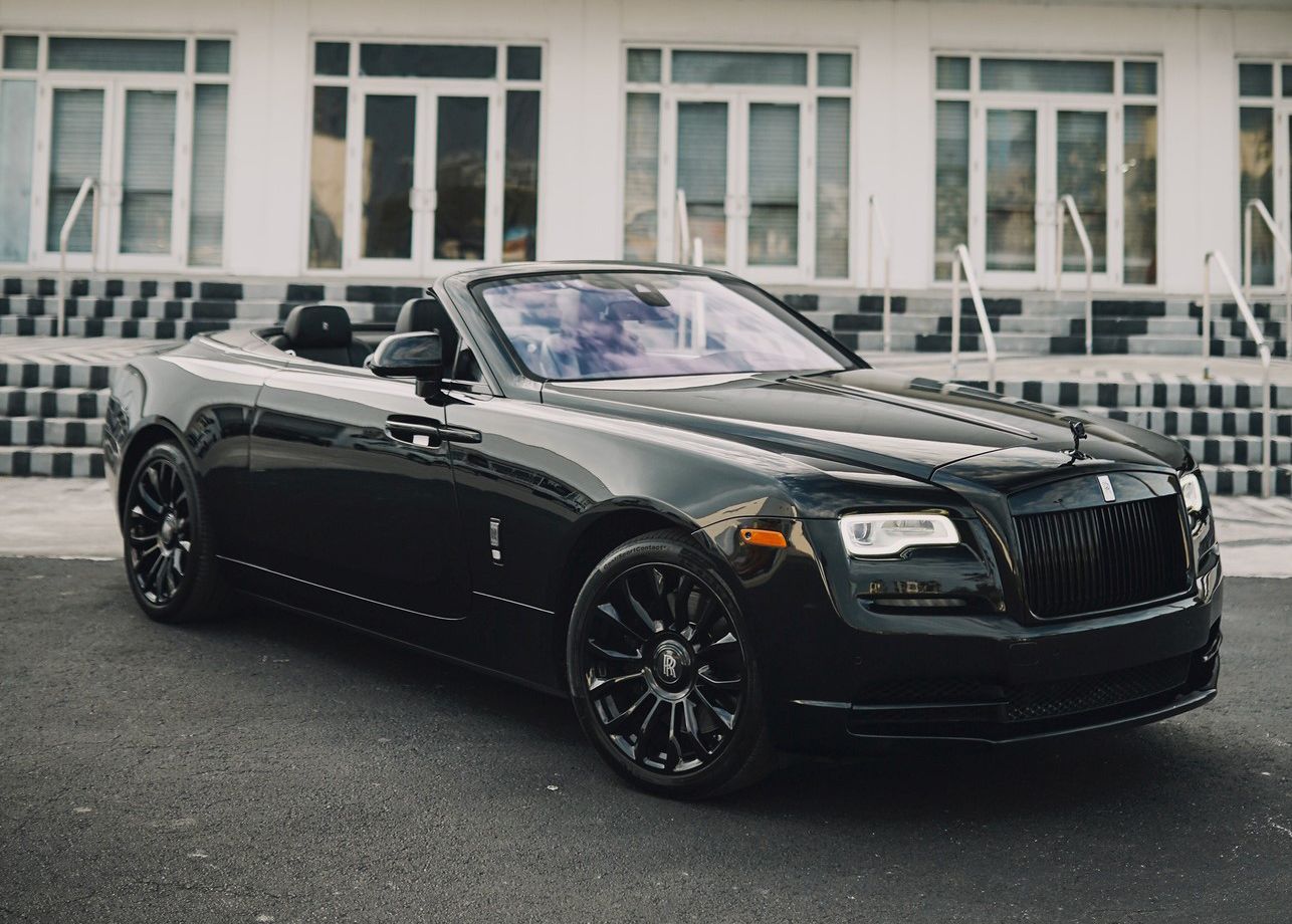 A black Rolls Royce wraith convertible is parked in front of a building.