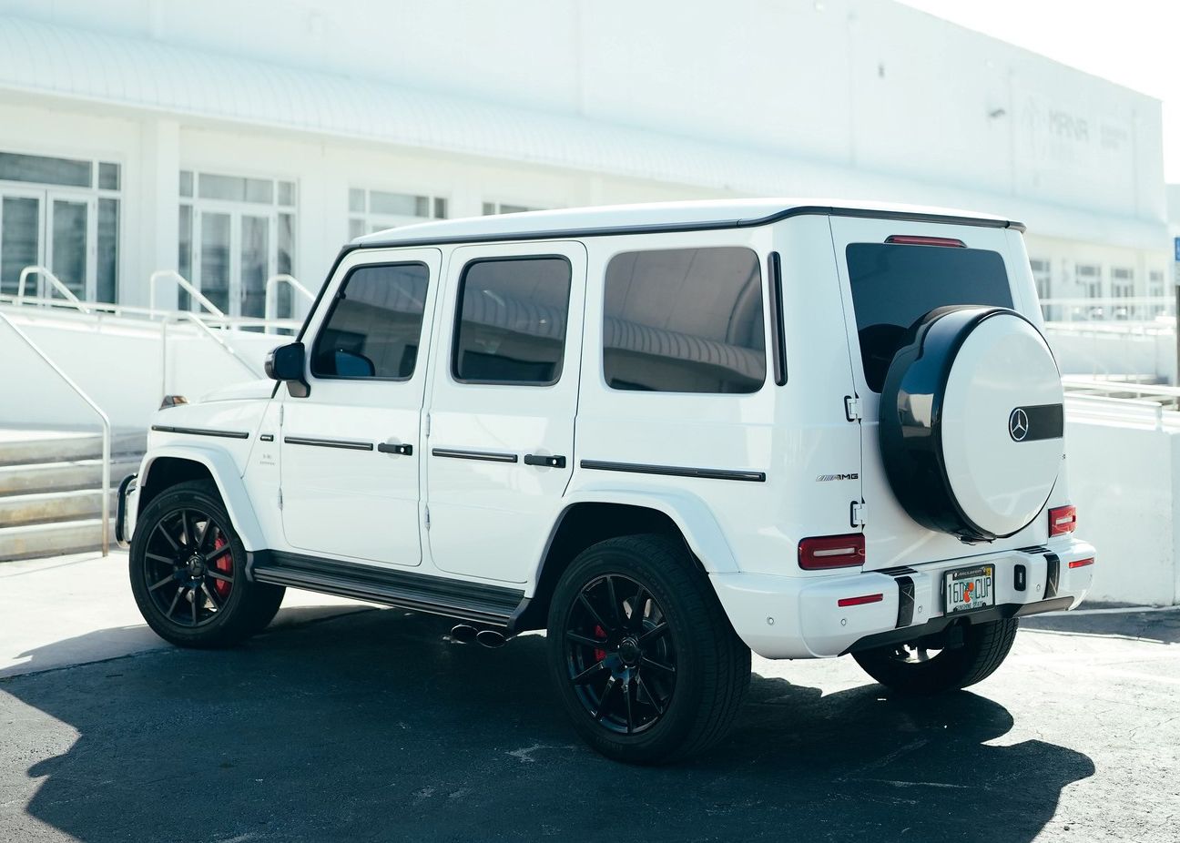 A white Mercedes Benz G550 is parked in front of a building.
