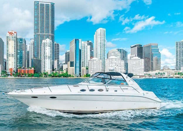 A white yacht is floating on top of a body of water in front of a city skyline.