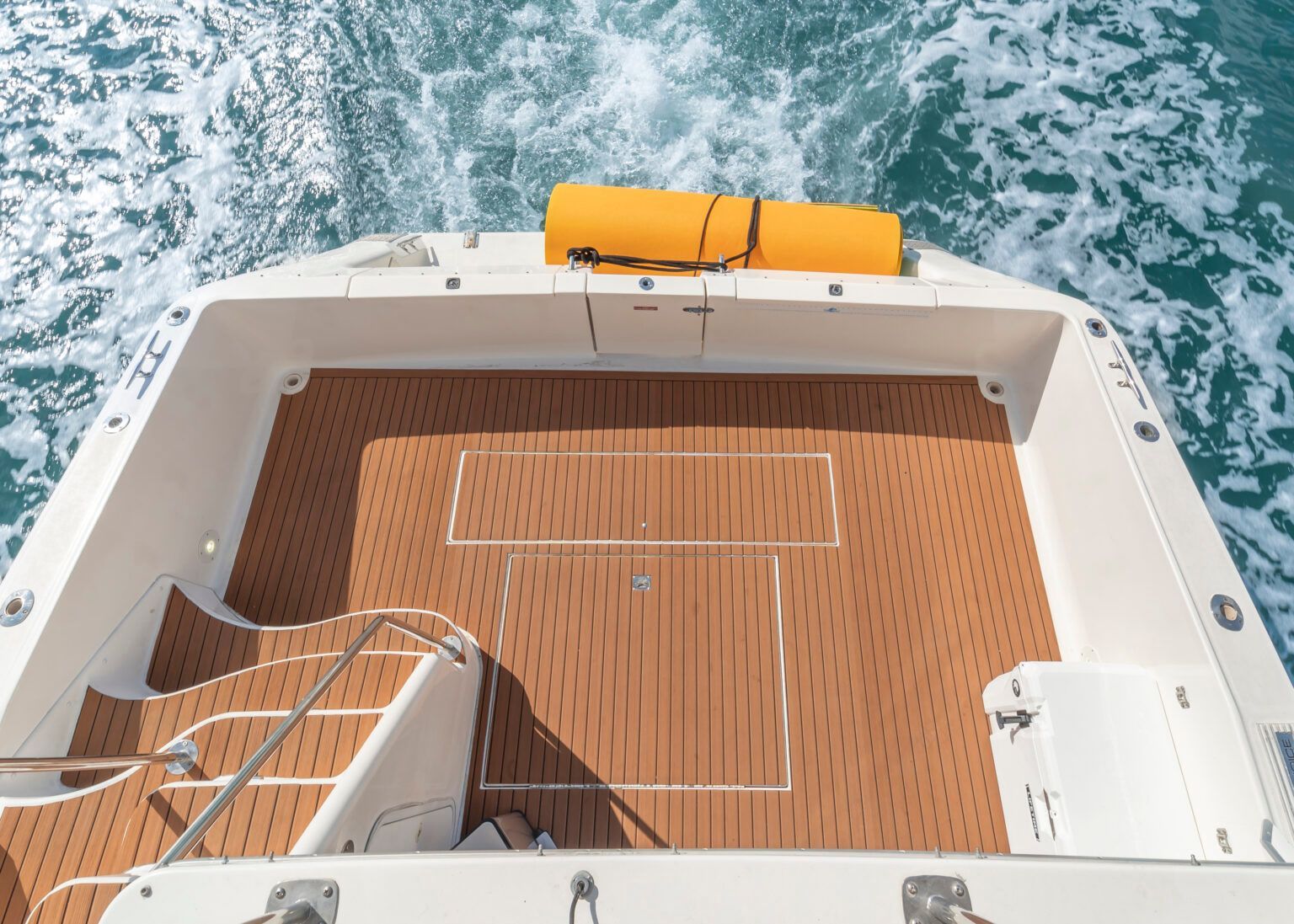 A white boat with a wooden deck is floating on top of a body of water.