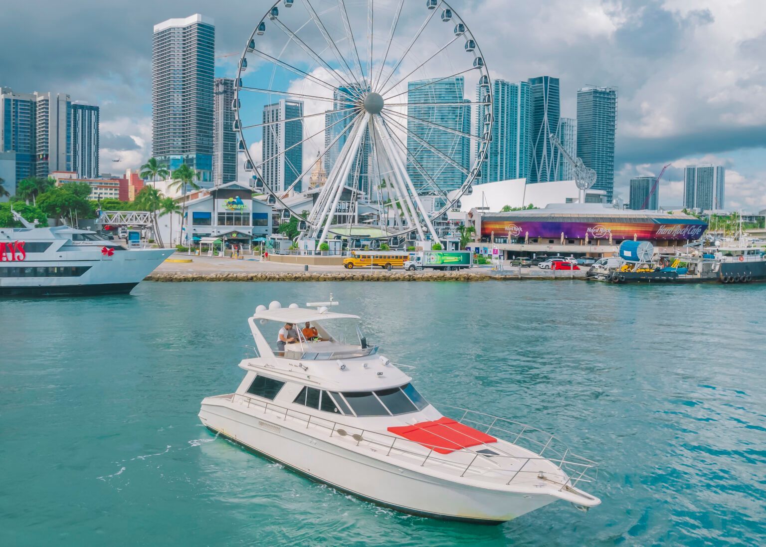 A white boat is floating on top of a body of water in front of a ferris wheel.