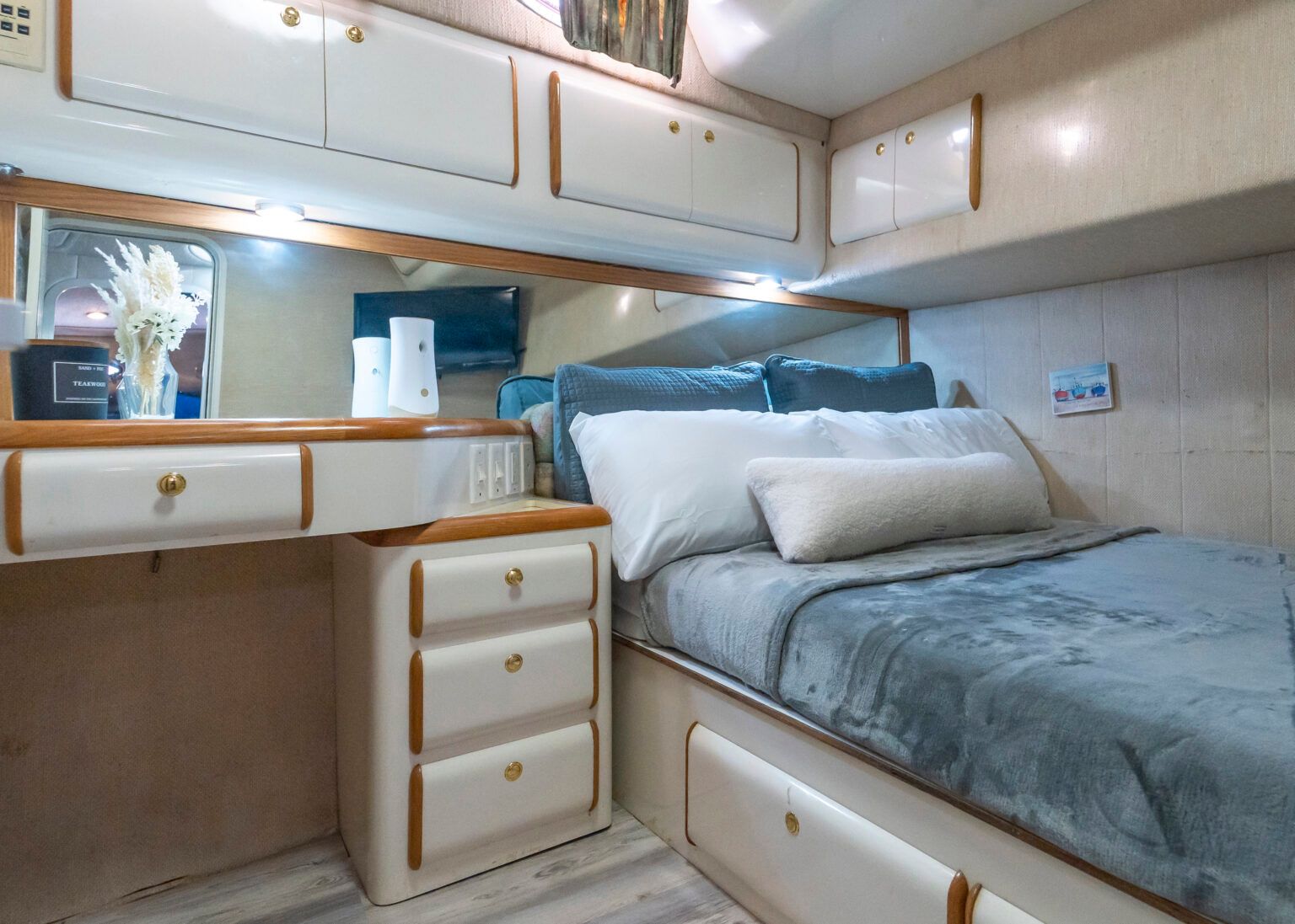 A bedroom on a boat with a bed, dresser and mirror.