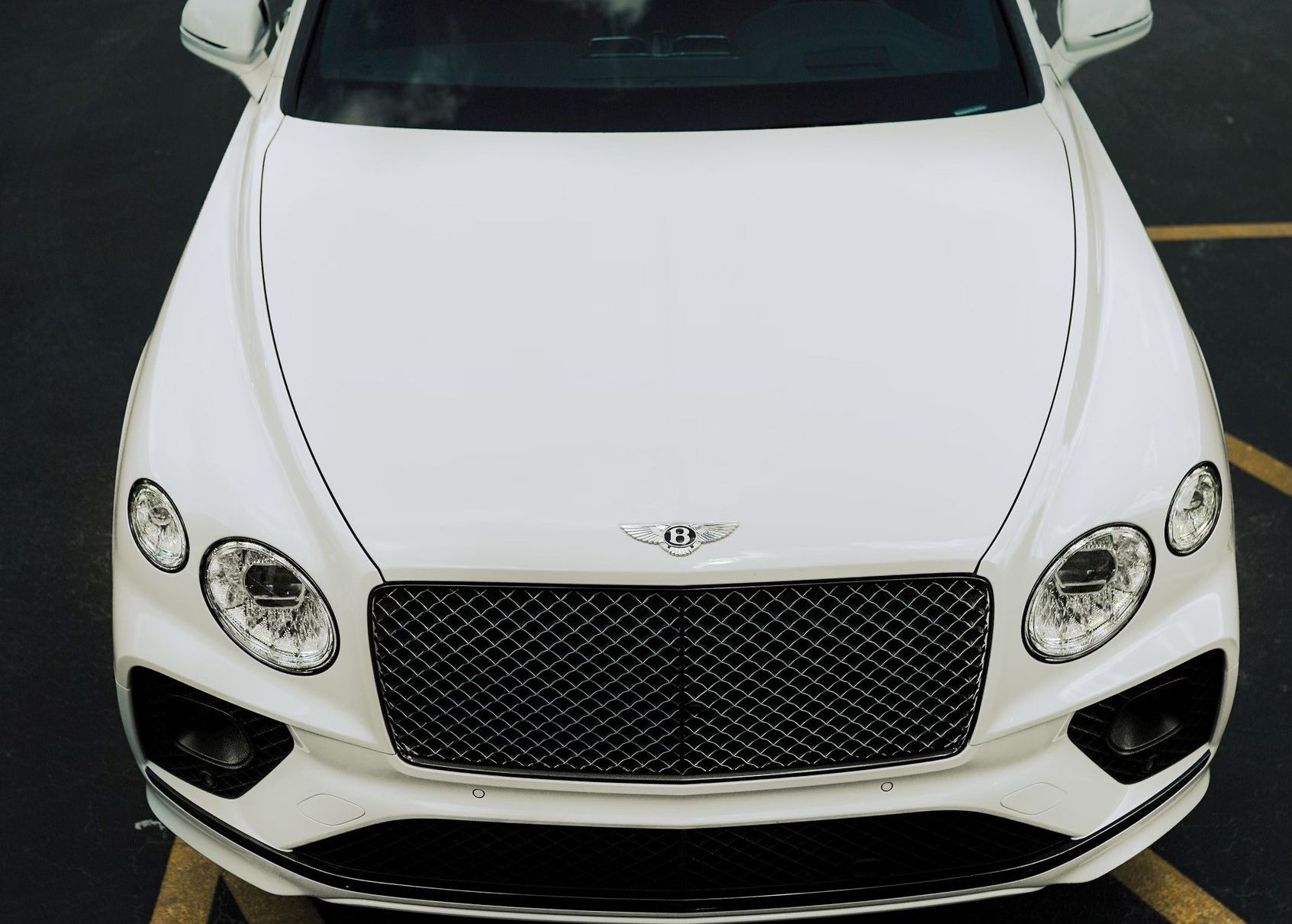 A white Bentley is parked in a parking lot.