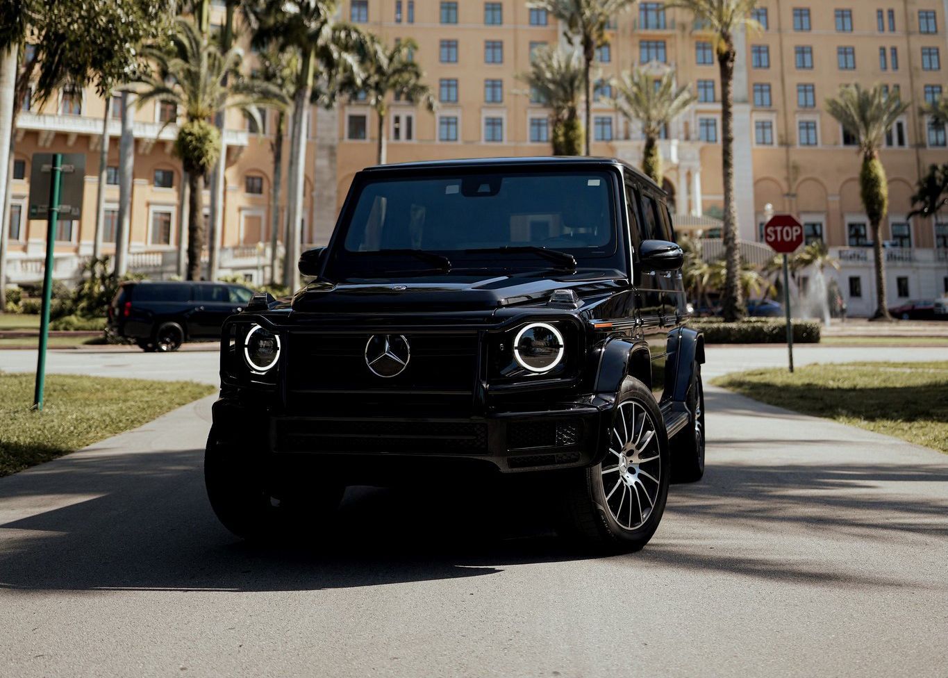 A black Mercedes Benz G550 is parked on a sidewalk in front of a building.