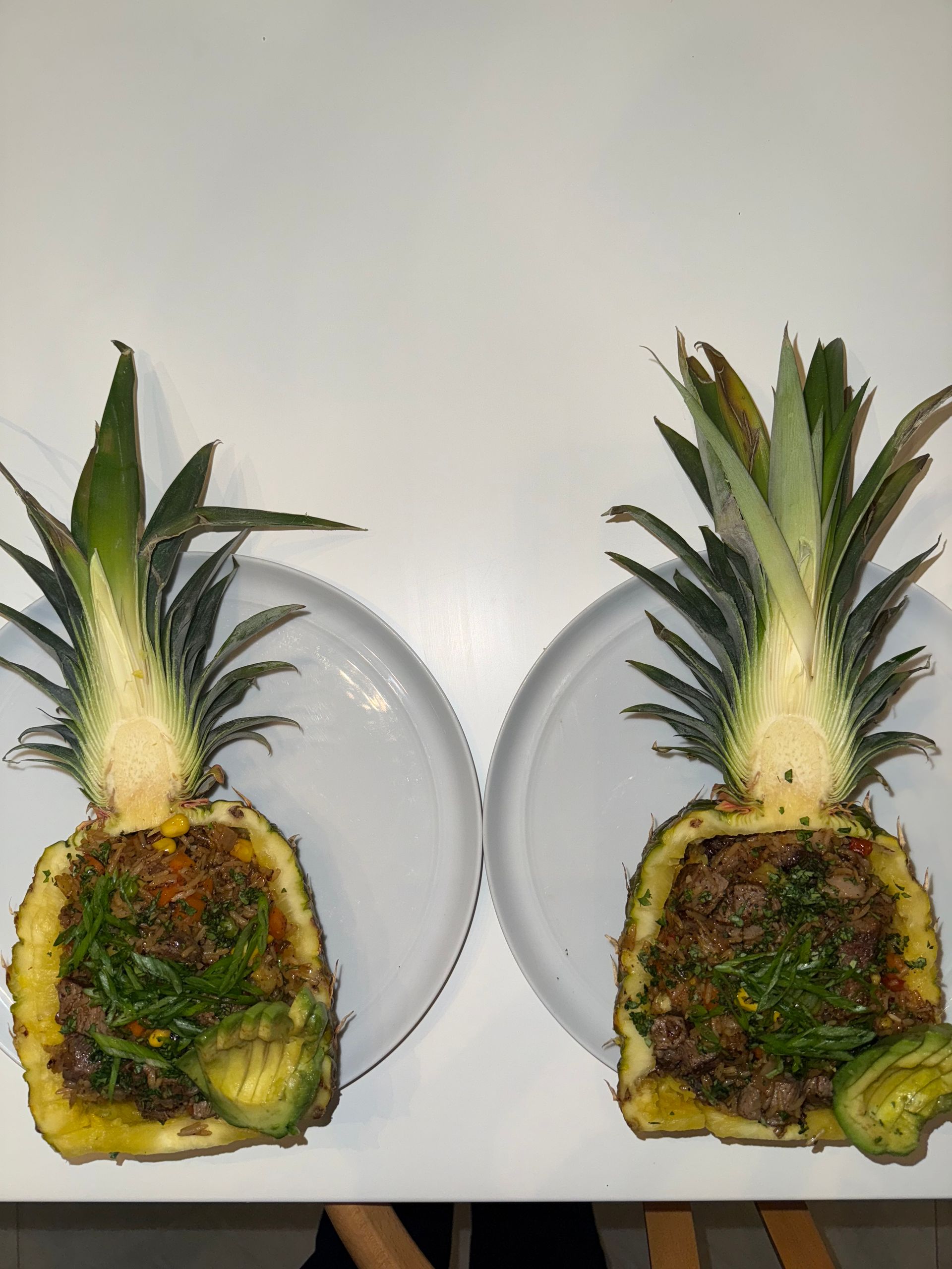 Two pineapples stuffed with meat and vegetables on white plates