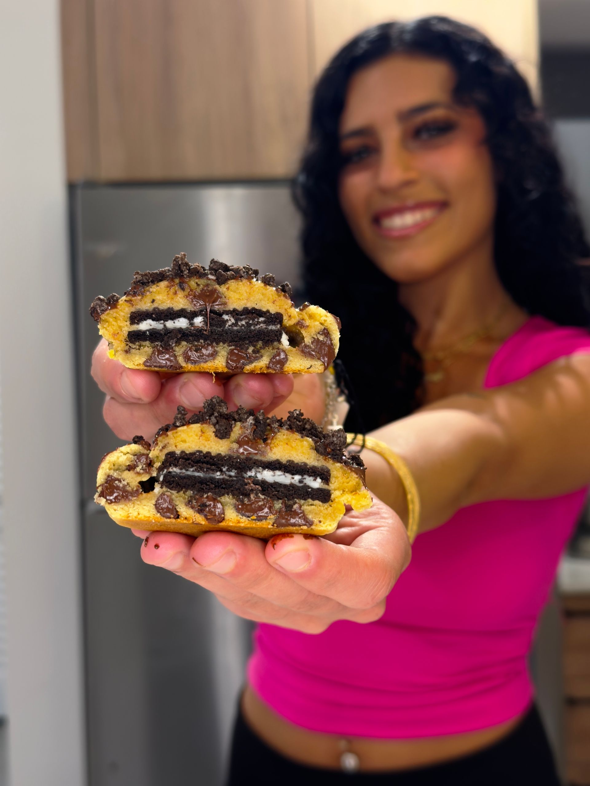 A woman in a pink top is holding two oreo cookies in her hands.