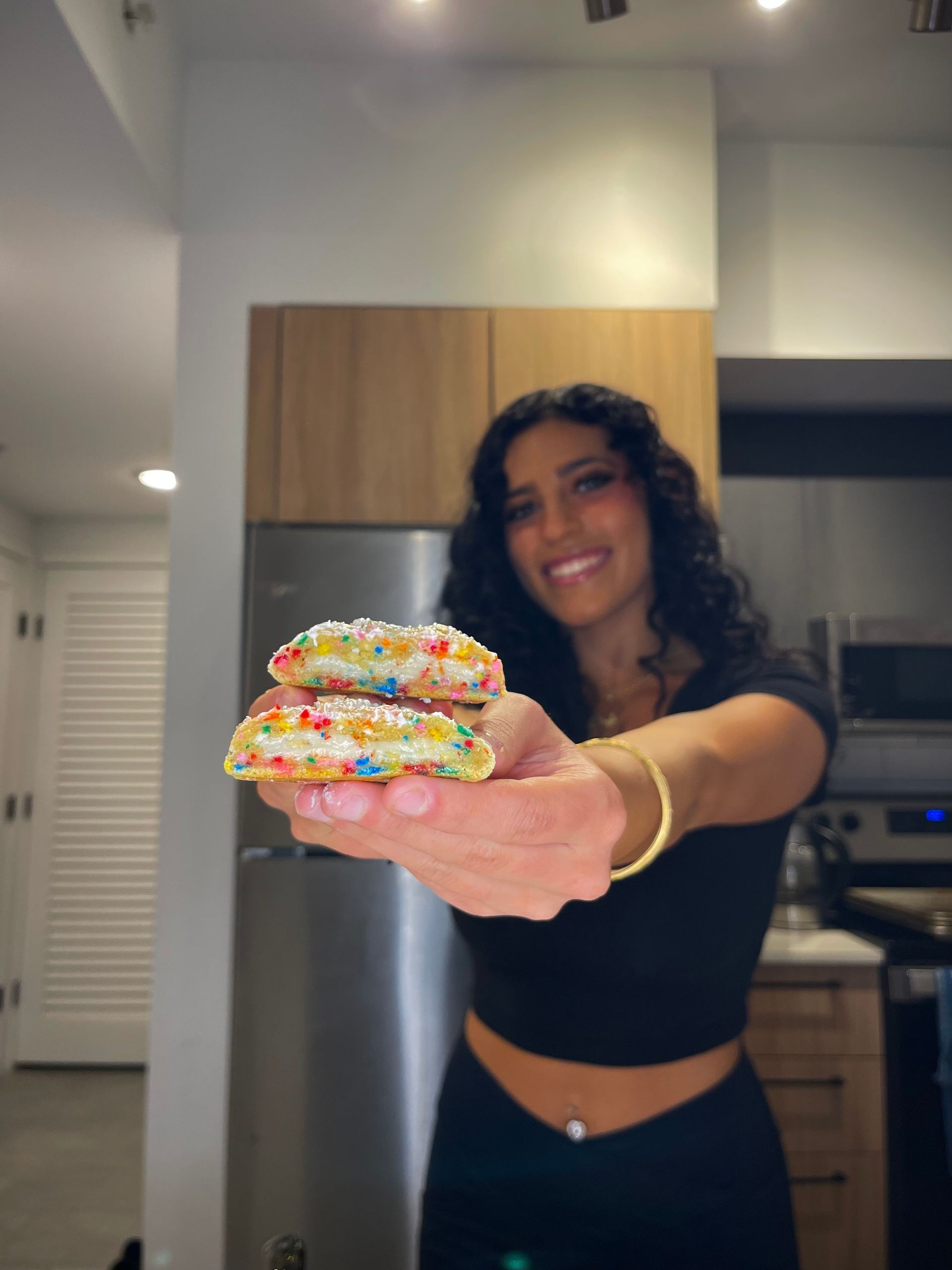 A woman is holding a stack of cookies with sprinkles on them.