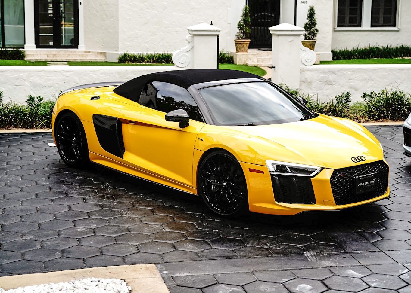A yellow Audi R8 convertible is parked in front of a house